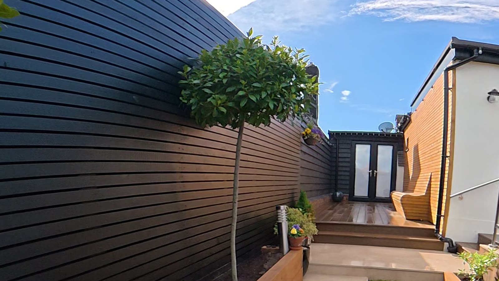 Black slatted fence along a path with steps up to a deck