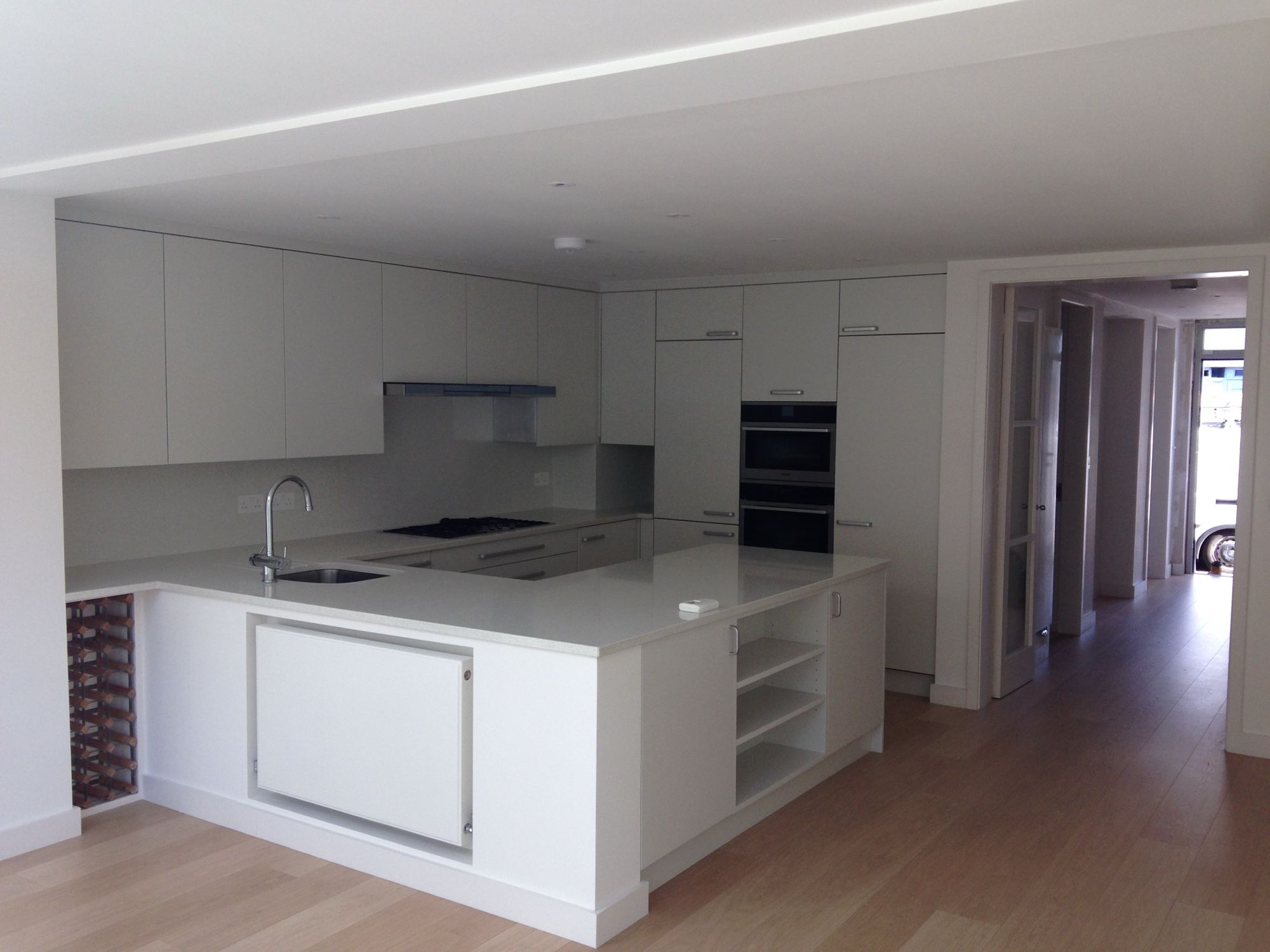 White handleless U-shaped kitchen with quartz worktops and oak floor