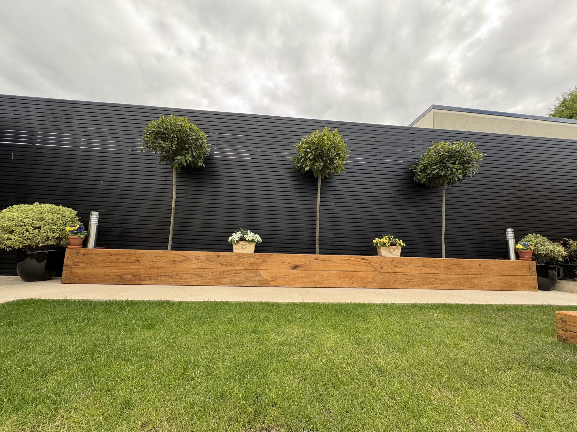 Long oak sleeper planter with standard bay trees against a black slatted fence